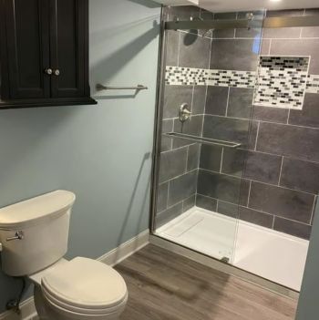 Modern bathroom with toilet, glass walk-in shower, gray tile, and wood-look flooring